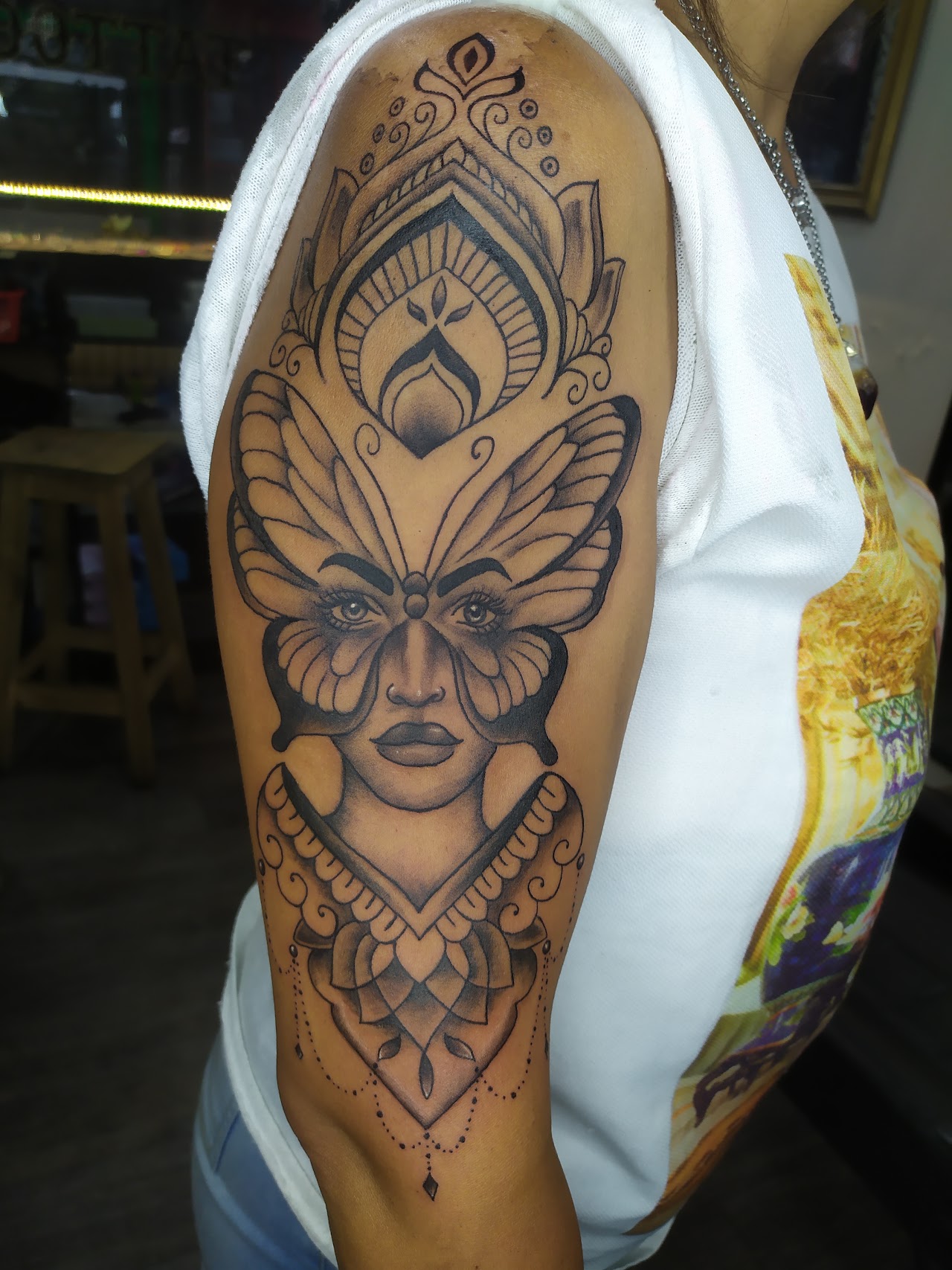 Tatuaje ornamental de mariposa y rostro, brazo